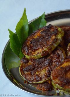 some food is sitting in a metal bowl on a white tablecloth and green leaves