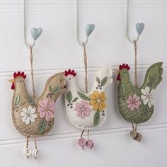 three birds hanging from hooks on a wall with flowers and hearts attached to the hooks