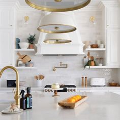 a kitchen with white cabinets and gold accents on the hood over the stove is filled with oranges