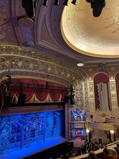 an auditorium filled with lots of people sitting on the stage and looking up at the ceiling