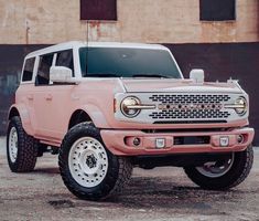 a pink truck is parked in front of a brick building and has white tires on it