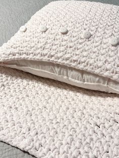 a white crocheted blanket laying on top of a bed next to a pillow