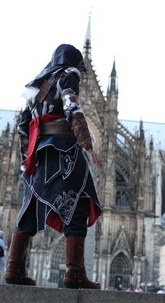 a man dressed in costume walking on the sidewalk near a castle with tall buildings behind him