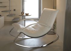 a white chair sitting in the middle of a living room next to a table and stairs