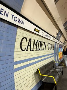 people are walking past a wall with the name camden town painted on it and benches in front of it