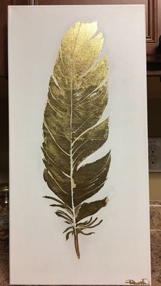 a gold leaf painted on a white canvas in front of a kitchen countertop with brown cabinets