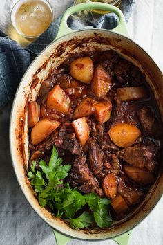 a pot filled with meat and potatoes on top of a table next to a glass of beer