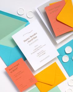 an assortment of different colored envelopes on top of white and blue paper with buttons