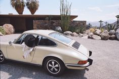 an old white porsche parked in front of a desert house with cactus and cacti