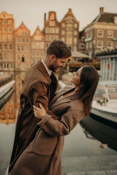 a man and woman standing next to each other in front of some boats on the water