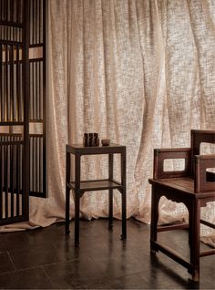 two wooden chairs sitting next to each other in front of a curtain