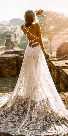 a woman in a white dress standing on top of a stone wall with her back to the camera