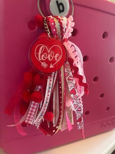 a red heart shaped keychain hanging from the side of a pink suitcase with love written on it