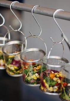 four glass containers filled with salad on a metal rack hanging from a wooden bar top