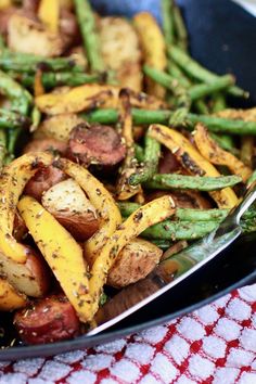 a pan filled with potatoes and asparagus on top of a red checkered table cloth