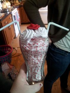 a person holding a glass filled with whipped cream on top of a wooden floor next to a kitchen counter