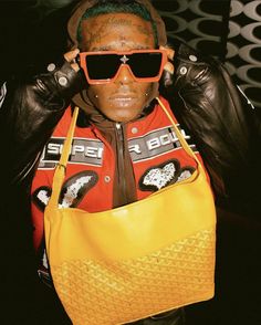 a man wearing sunglasses and holding a yellow bag in front of his face with both hands