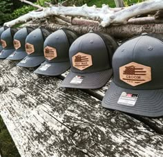 several hats are lined up on a bench in front of some logs and branches with the word bloom written on them