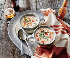 two bowls of soup are sitting on a plate with spoons and a bottle of beer