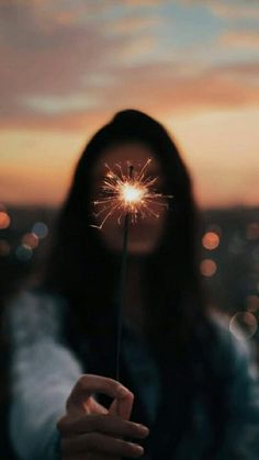 a woman holding a sparkler in front of her face with the sun setting behind her