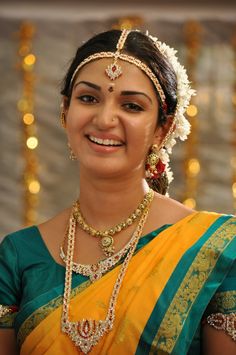 a woman in a yellow and green sari with jewelry on her head, smiling at the camera