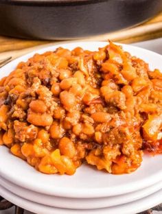 a white plate topped with beans and meat next to a skillet filled with sauce