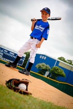 a young boy holding a baseball bat standing on top of a dirt field next to a catchers mitt