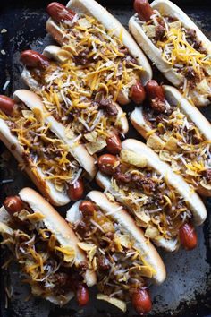 several hot dogs with toppings on them sitting in a black tray, ready to be eaten