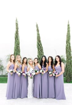 a group of women standing next to each other wearing purple dresses and holding bouquets