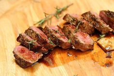 some meat is sitting on top of a wooden cutting board and garnished with herbs