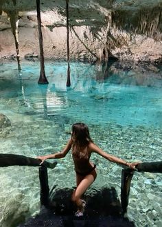 a woman in a bathing suit standing at the edge of a pool with clear water