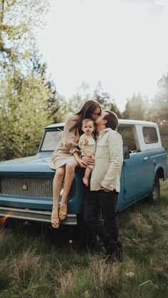 a man and woman are kissing in front of an old blue truck with their child