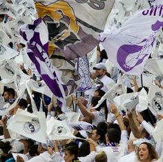 a large group of people holding flags and waving them in the wind at a sporting event