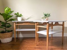 two wooden tables with plants on them in front of a white wall and wood floor