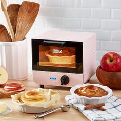 a pink toaster oven sitting on top of a wooden table next to apples and cinnamons