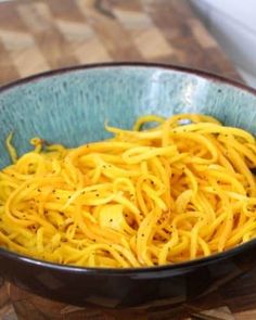 a blue bowl filled with yellow noodles on top of a wooden cutting board next to a knife