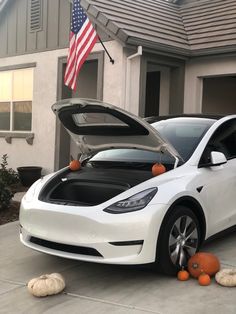 an electric car is parked in front of a house with pumpkins on the ground