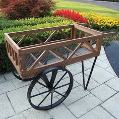 a wooden wagon sitting on top of a brick walkway next to flowers and bushes in the background