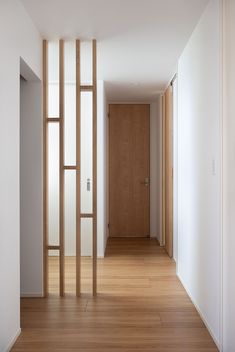 an empty hallway with wooden floors and white walls, leading to a door that leads to another room