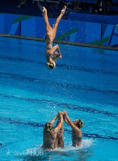 three men are in the swimming pool and one is jumping up into the water to catch a frisbee