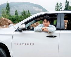 a man sitting in the drivers seat of a white car with mountains in the background