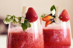 two glasses filled with fruit and garnish on top of a table