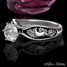 a close up of a ring with a flower on the side and a rose in the background