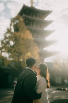 a man and woman standing next to each other in front of a tall pagoda tower