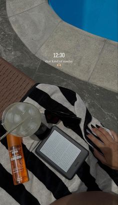 a woman is sitting by the pool using her tablet