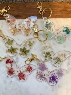 six glass keychains with flowers and butterflies on them sitting on a marble slab