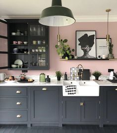 a kitchen with pink walls and black cabinets, white sink and green potted plants