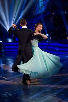 two people are dancing on the dance floor with their arms around each other and lights behind them