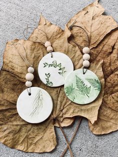 three handmade ceramic discs sitting on top of a leaf covered ground next to two wooden beads