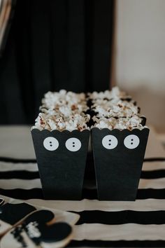 two black boxes filled with popcorn sitting on top of a striped tablecloth covered table